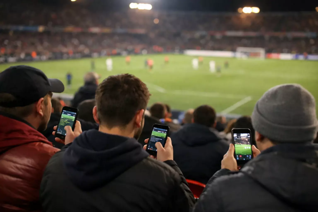 Voetbalfans in een stadion die de wedstrijd volgen terwijl ze op hun smartphones kijken